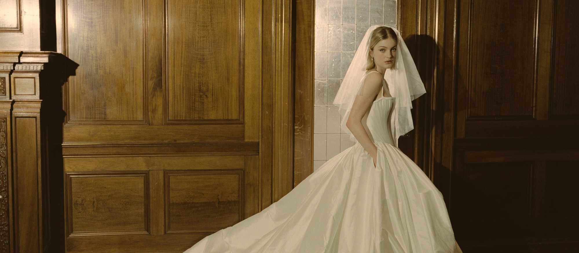 Bride in a structured satin gown in a sunlit bridal atelier
